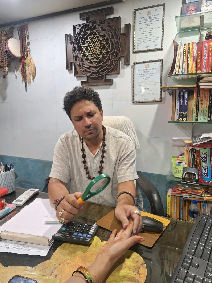 Acharya ji reading a palm with a magnifying glass